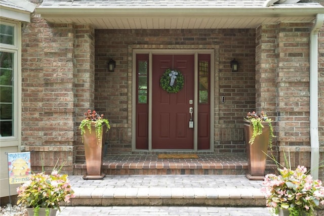 view of exterior entry with a shingled roof, a porch, and brick siding