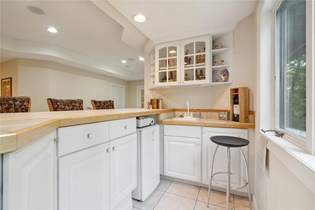 kitchen featuring recessed lighting, light countertops, glass insert cabinets, white cabinetry, and a sink