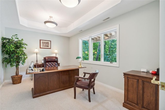 office space with light carpet, visible vents, a tray ceiling, and baseboards