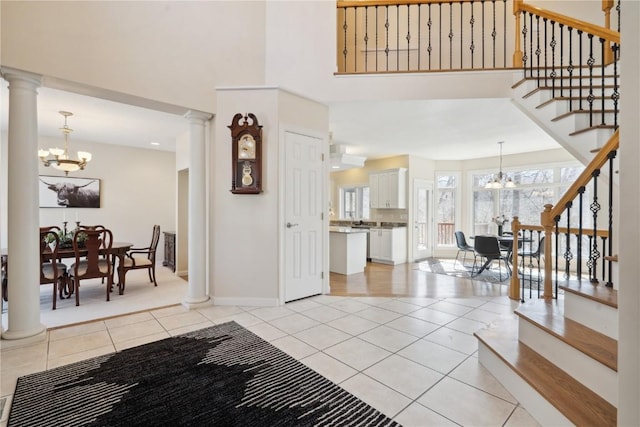 entryway featuring light tile patterned flooring, decorative columns, stairway, and an inviting chandelier