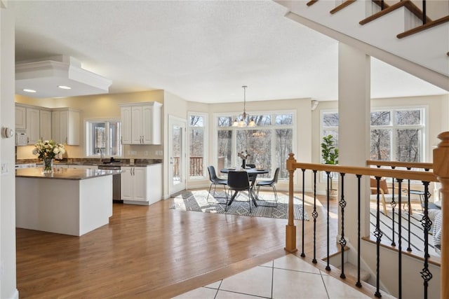 kitchen with a wealth of natural light, dark countertops, dishwasher, and an inviting chandelier