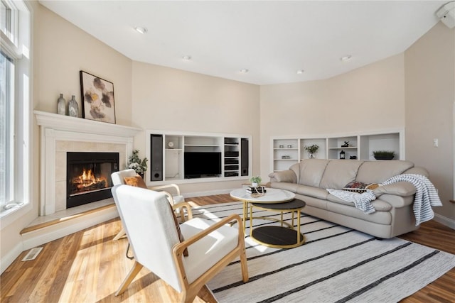 living area featuring baseboards, visible vents, wood finished floors, and a tile fireplace