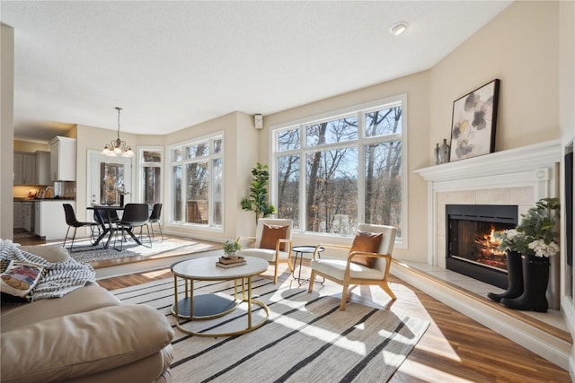 living room with a chandelier, a tiled fireplace, and wood finished floors