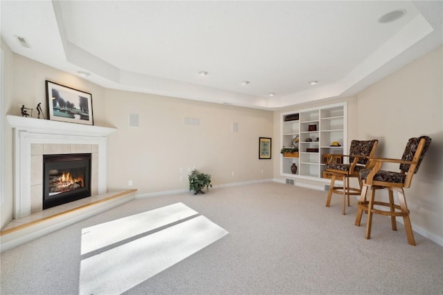 sitting room featuring a tile fireplace, visible vents, baseboards, a tray ceiling, and carpet