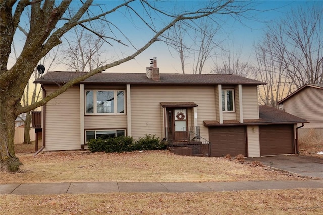 raised ranch featuring an attached garage, a chimney, and driveway