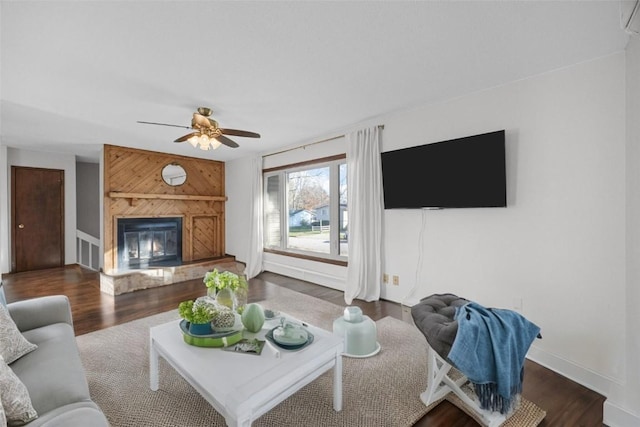 living area featuring a glass covered fireplace, ceiling fan, baseboards, and wood finished floors