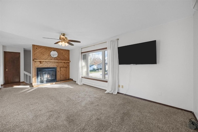 unfurnished living room with wooden walls, ceiling fan, baseboards, carpet, and a glass covered fireplace