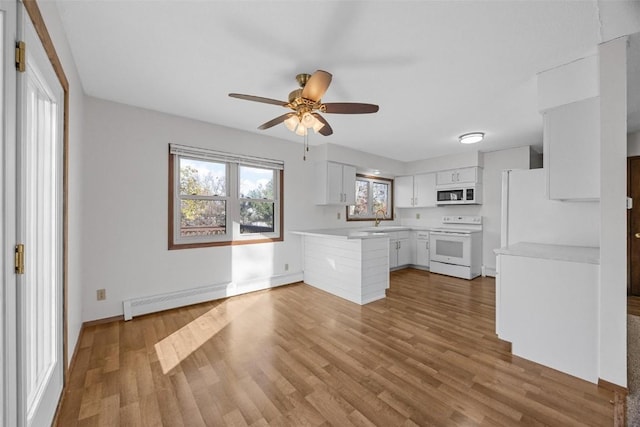 kitchen with white appliances, wood finished floors, a sink, light countertops, and white cabinetry