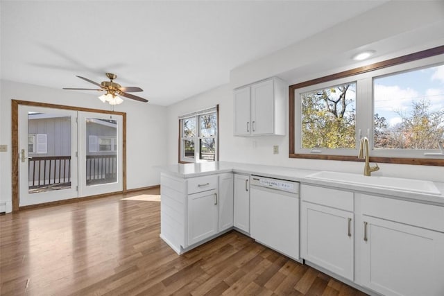 kitchen featuring a peninsula, white dishwasher, dark wood-style flooring, a sink, and white cabinetry