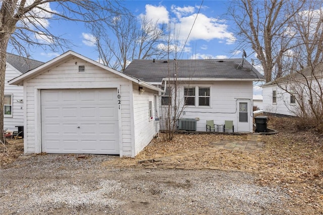 back of house with central air condition unit, a shingled roof, dirt driveway, and an outbuilding