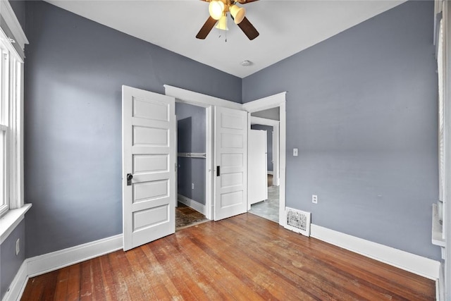 unfurnished bedroom with a ceiling fan, hardwood / wood-style flooring, visible vents, and baseboards