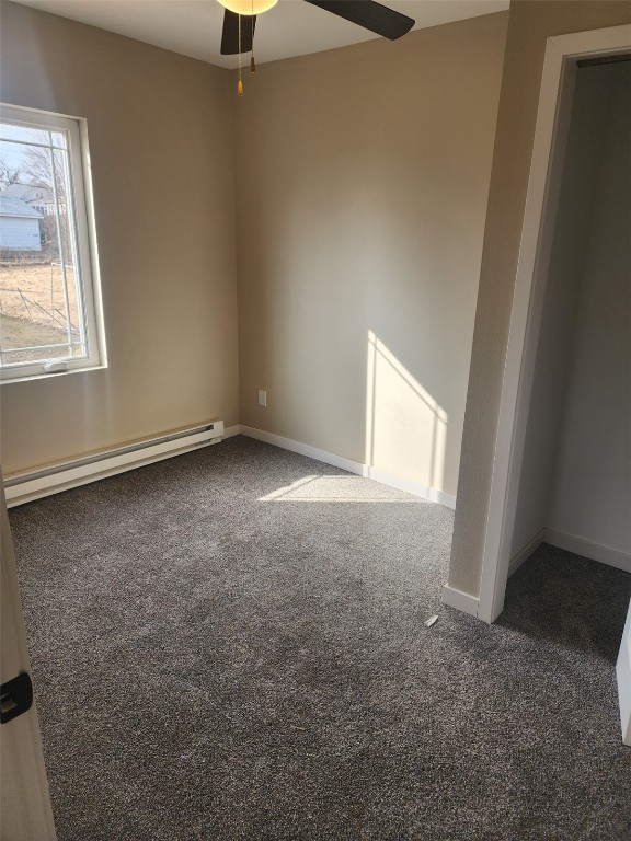 empty room featuring carpet, ceiling fan, a baseboard radiator, and baseboards