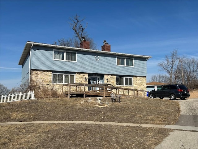 view of front of house featuring a chimney, stone siding, fence, and a deck