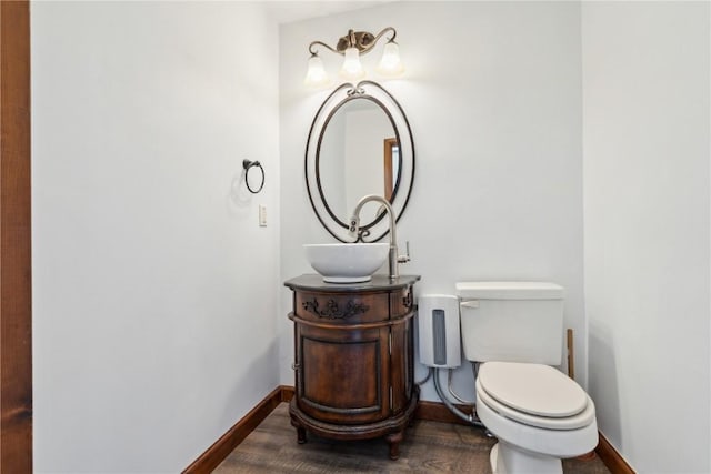 half bathroom with toilet, vanity, baseboards, and wood finished floors