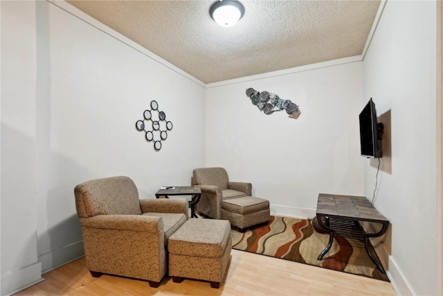 sitting room with a textured ceiling, baseboards, wood finished floors, and crown molding