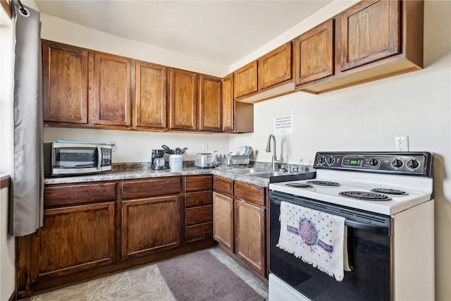 kitchen featuring brown cabinets, stainless steel microwave, a sink, and electric range