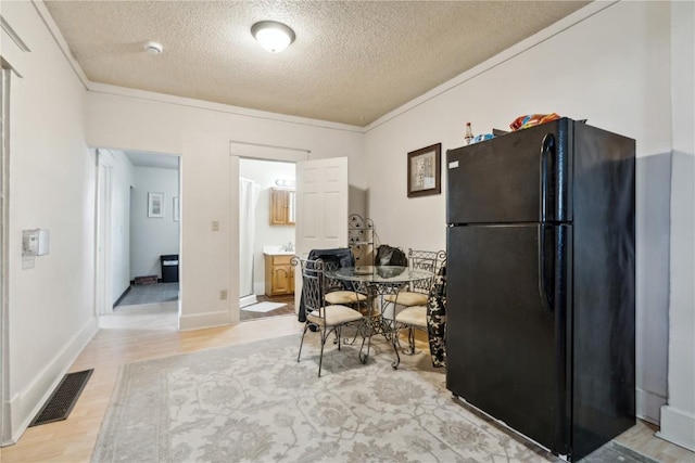 kitchen featuring visible vents, light wood-style floors, freestanding refrigerator, ornamental molding, and a textured ceiling