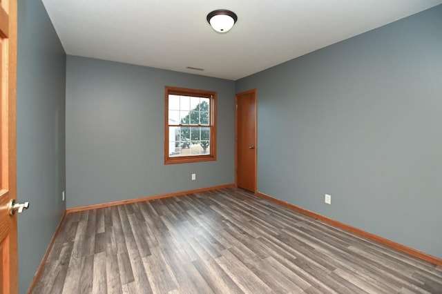 empty room featuring wood finished floors, visible vents, and baseboards