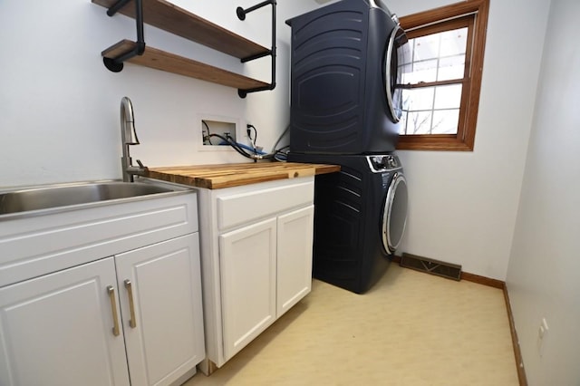 washroom featuring stacked washer / drying machine, cabinet space, visible vents, a sink, and baseboards