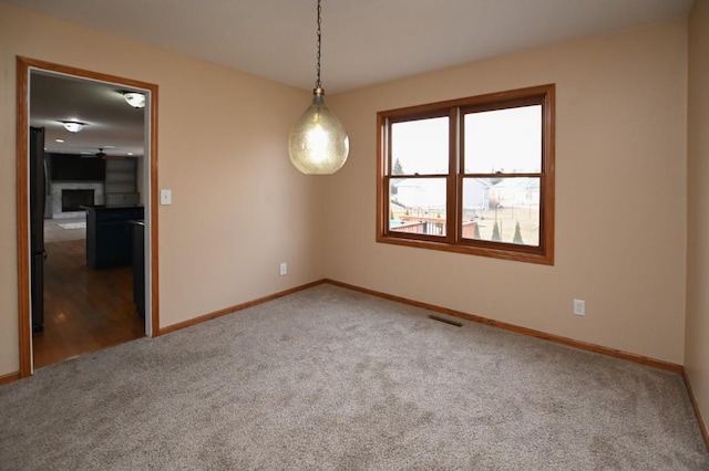 carpeted empty room with baseboards, visible vents, and a fireplace with raised hearth