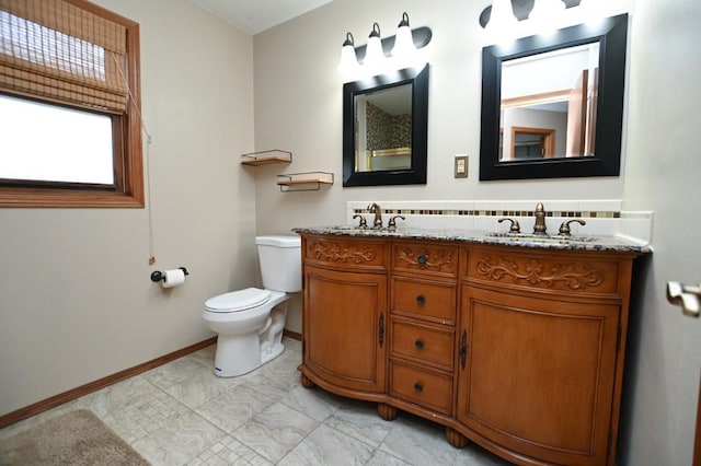 bathroom featuring toilet, double vanity, baseboards, and a sink