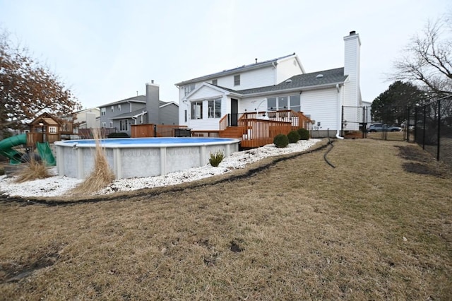 back of property featuring an outdoor pool, a lawn, a chimney, fence, and a wooden deck