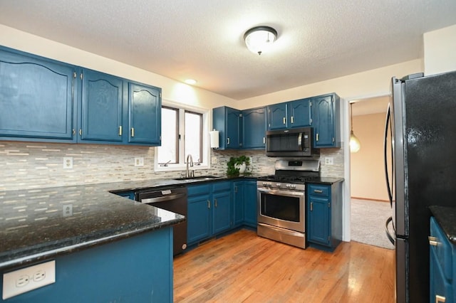 kitchen with light wood-style flooring, blue cabinets, stainless steel appliances, a sink, and backsplash