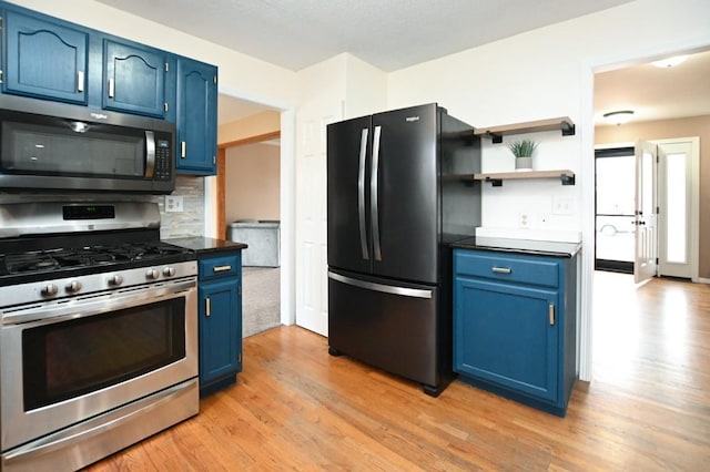 kitchen featuring dark countertops, light wood-style flooring, stainless steel appliances, blue cabinetry, and backsplash