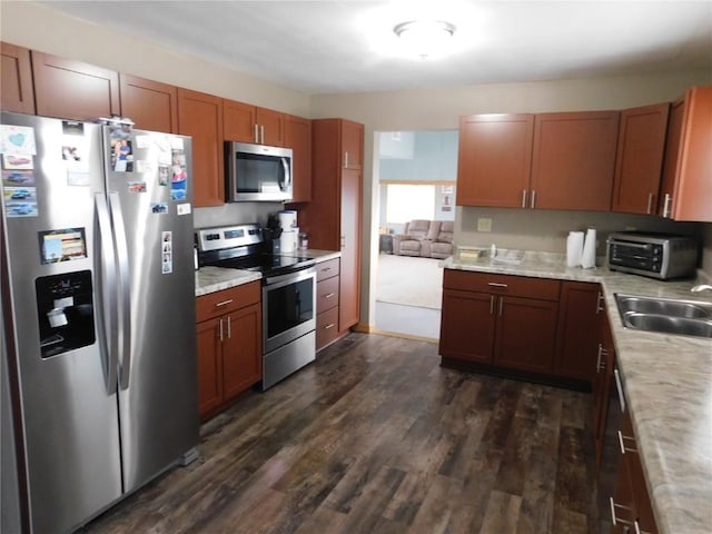 954 Monroe Ave, Tipton, IA 52772 - kitchen with appliances with stainless steel finishes, light countertops, dark wood-type flooring, a sink, and brown cabinetry