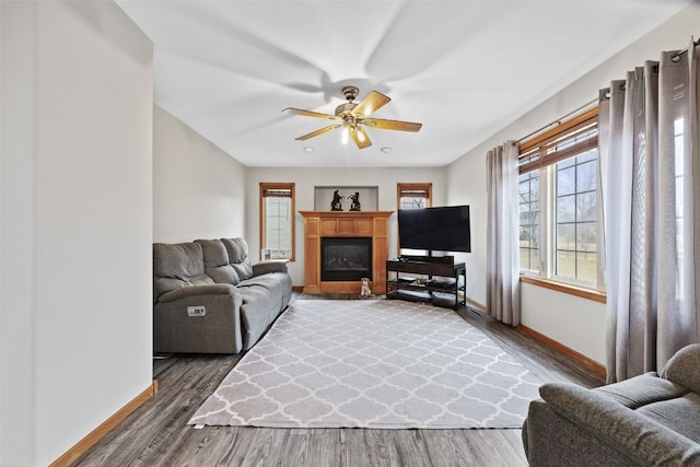 living room featuring a glass covered fireplace, wood finished floors, a ceiling fan, and baseboards