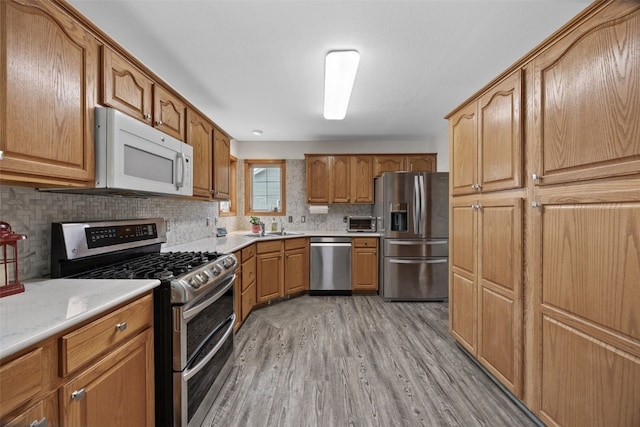 kitchen with brown cabinetry, decorative backsplash, light wood-style flooring, appliances with stainless steel finishes, and a sink