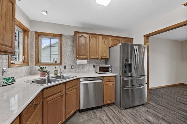 kitchen featuring light wood finished floors, appliances with stainless steel finishes, a sink, light countertops, and backsplash