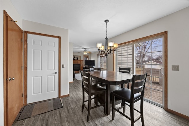 dining room featuring an inviting chandelier, baseboards, wood finished floors, and a glass covered fireplace