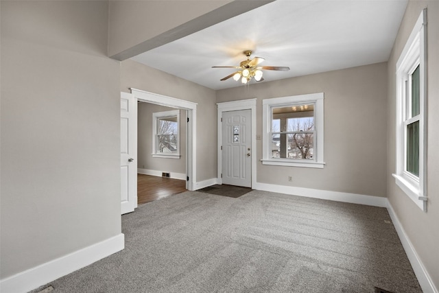 foyer entrance with ceiling fan, dark carpet, a wealth of natural light, and baseboards