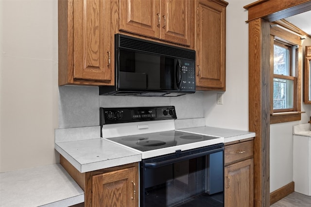 kitchen with brown cabinets, electric stove, light countertops, and black microwave