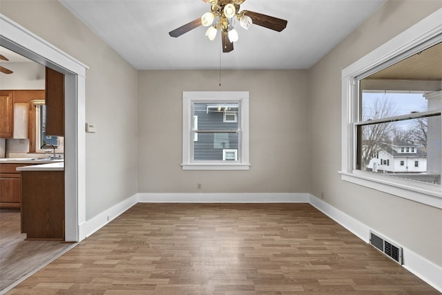 unfurnished room with light wood-style floors, baseboards, visible vents, and a ceiling fan