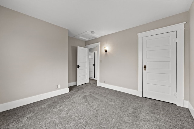 carpeted empty room with attic access and baseboards