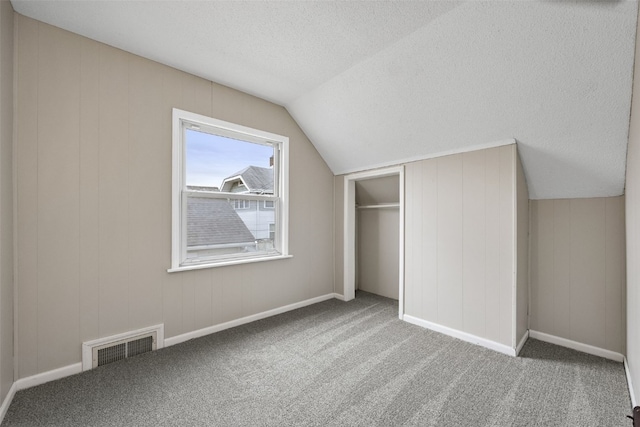 additional living space featuring a textured ceiling, carpet flooring, visible vents, and lofted ceiling