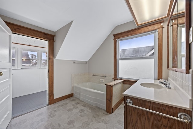 bathroom featuring lofted ceiling, vanity, baseboards, and a bath