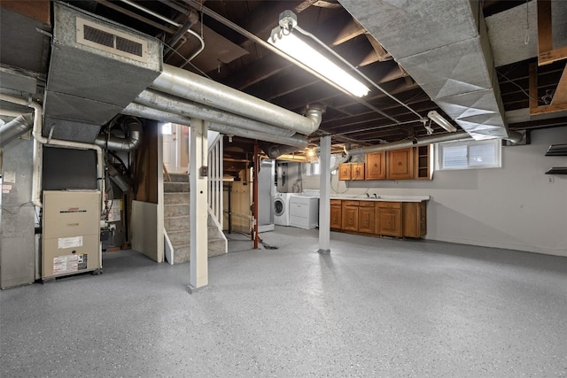 below grade area featuring visible vents, heating unit, stairs, washing machine and dryer, and a sink