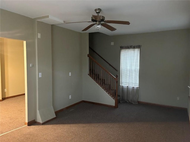 carpeted empty room featuring ceiling fan, stairway, and baseboards