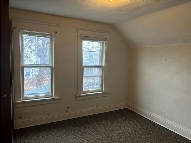 additional living space featuring dark carpet, vaulted ceiling, and baseboards