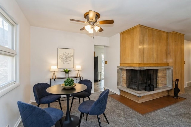 interior space with a ceiling fan, baseboards, a wealth of natural light, and a stone fireplace