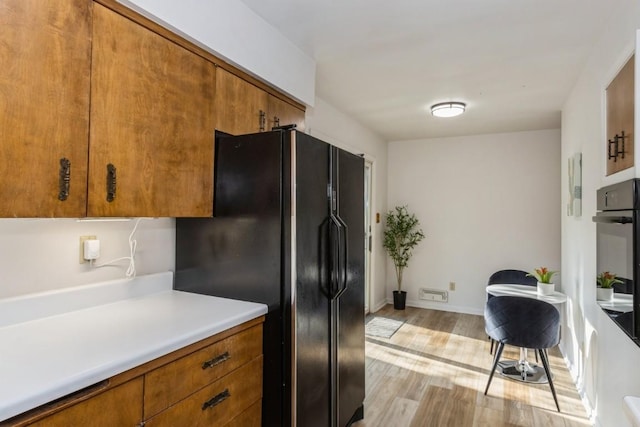 kitchen featuring black appliances, brown cabinetry, light countertops, and light wood-style flooring