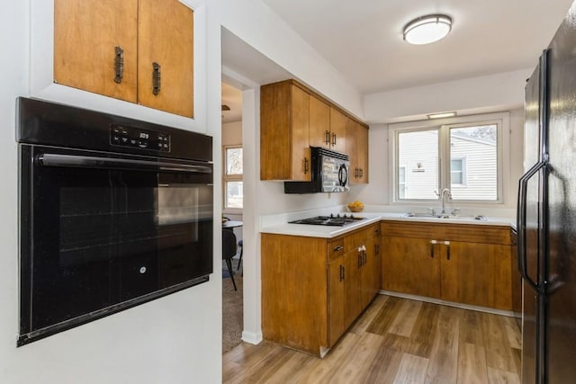 kitchen with a sink, light wood-style floors, light countertops, brown cabinets, and black appliances