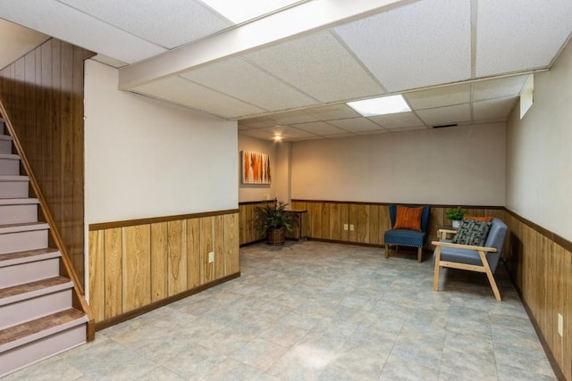 living area featuring a drop ceiling, a wainscoted wall, wood walls, stairway, and tile patterned floors