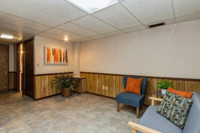 sitting room with a wainscoted wall, wood walls, visible vents, and a drop ceiling