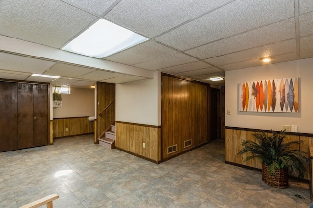 finished basement with a wainscoted wall, wood walls, and a paneled ceiling