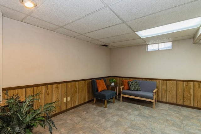 living area with a wainscoted wall, wooden walls, visible vents, and a drop ceiling