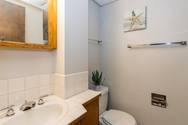 half bath with backsplash, vanity, and toilet